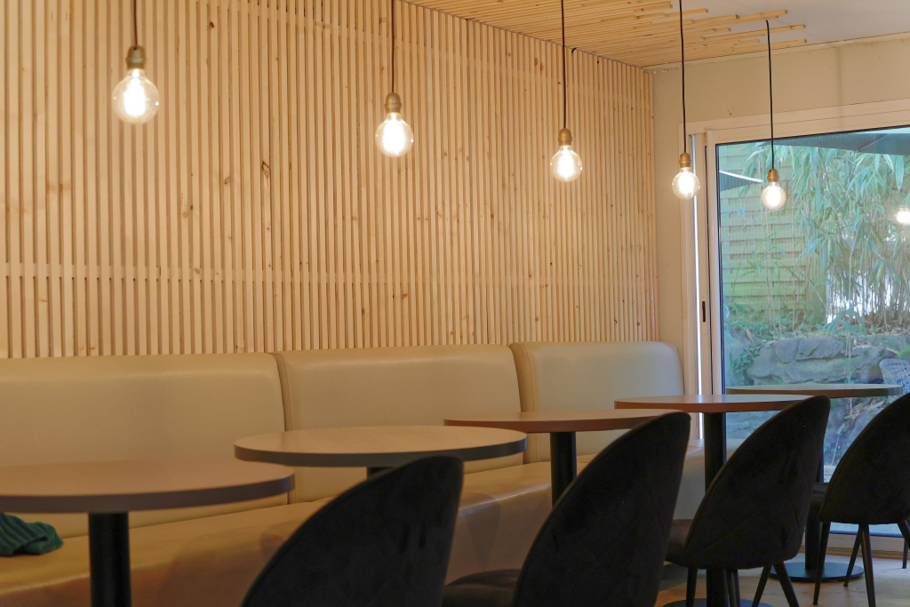 rénovation cantine sol mur et plafond ambiance chaleureuse grâce au bardage en bois sur le mur et le plafond, coloris clairs pour redonner de la lumière à la pièce augmenter les sources de lumières au dessus de chaque table et installation de  leds sur la zone de détente recyclage du mobilier de l'hôtel récupéré après les travaux : les banquettes, les tables, les chaises, le parquet, le meuble de rangement