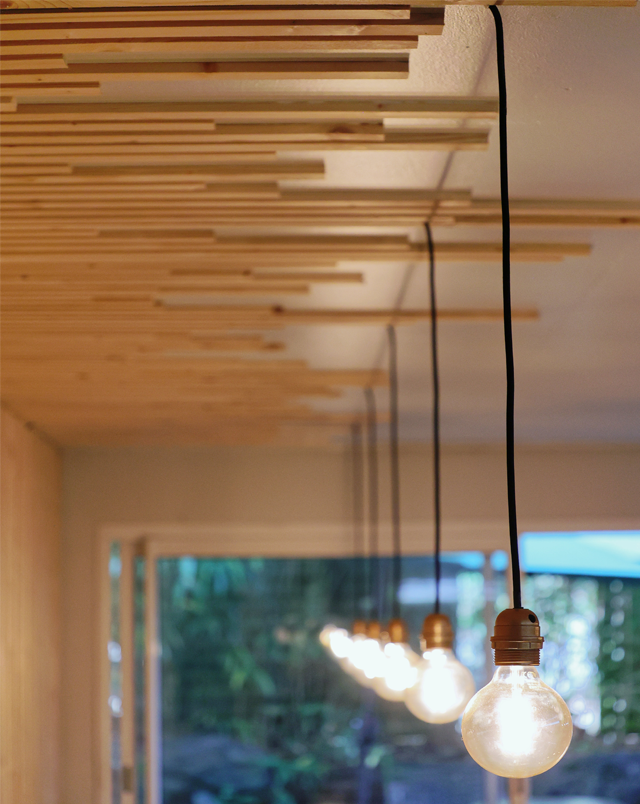 réalisation bardage bois mur et plafond avec les luminaires suspendus aux éléments en bois du bardage créant un décor très géométrique et très aligné. les éléments sont contrastés par la couleur claire du bois et le noir du fil électrique