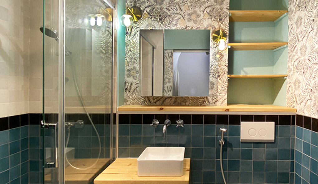 petite salle de bain rénovation réduction des éléments de la vasque pour augmenter la circulation installation douche tablette bois vasque carrée zellige bleu turquoise et zellige noir papier peint spécial salle de bain végétal blanc et noir installation d'une douchette de toilette réhausse luminaires en laiton doré étagères bois peinture bleue des lacs